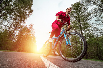 A man in a tracksuit on a bicycle rides on a road in the forest. The concept of a healthy lifestyle, cardio training. Copyspace.