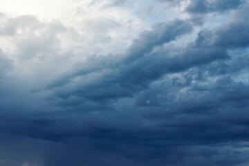 Dramatic rainy clouds on dark blue stormy evening sky. Natural background with stormclouds and sunlights of setting sun.