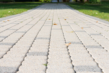 Fototapeta premium Empty stone pedestrian road with green grass on two sides of it.