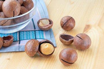 Pile of macadamia nuts in whole kernels and half opened on wooden background with blue napkin and translucent bowl. Seeds of the australian nuts also known as macadamia. 