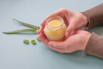 Young female hands are holding translucent glass jar with cream made of wax and aloe essence.Revitalizing soft cream as organic moisturizer.