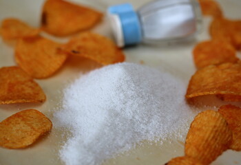 Stack of salt on wooden table surrounded by pepper chips, salt sellar in soft focus
