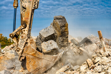 Excavator bucket filled with soil, stones and pieces of concrete