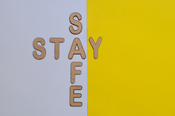 Stay safe message with 3d wooden alphabet letters in crossword pattern placed on a pair of solid color background. Pandemic situation advice. Top view.