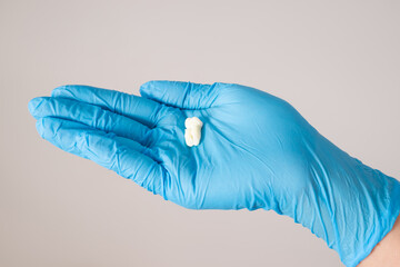 Wisdom teeth extraction, close-up tooth on gloved hand on gray background