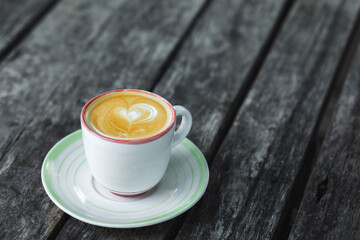 Cup of fresh creamy cappuccino with heart latte art on foam. Background of black dark wooden table with shabby aged surface. Empty space.