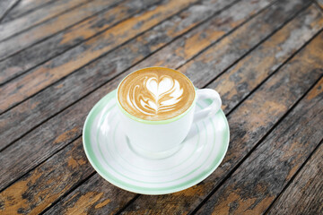 Cup of fresh creamy cappuccino with latte art on foam. Background of brown wooden table with shabby aged surface. View from above.