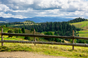 Fototapeta na wymiar fence on the hill in rural area. early autumn scenery in carpathian mountains. sunny weather with clouds on the sky. hills rolling in tho the distant mountain ridge