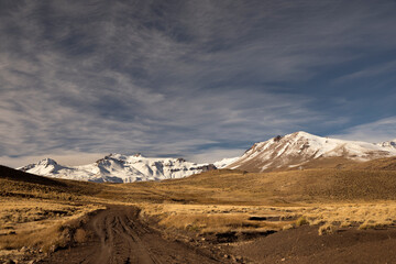 Adventure. Traveling along the dirt road across the yellow meadow, towards volcano Domuyo in the snowy mountains. 