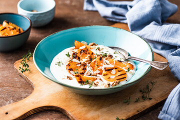Breakfast bowl with grilled apricots with natural yoghurt, walnuts, almonds and thyme. Wodden background.