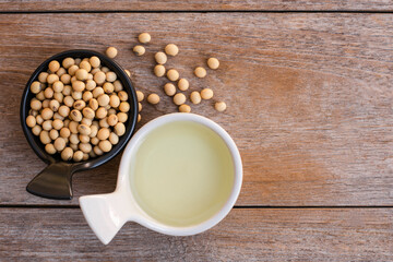 Soy bean oil with soybean seeds in black and white ceramics bowl isolated on rustic wood table background. Overhead view. Flat lay. 
