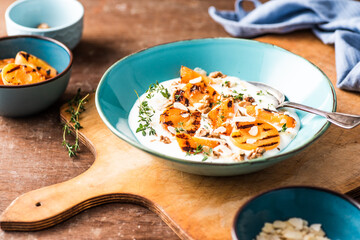 Breakfast bowl with grilled apricots with natural yoghurt, walnuts, almonds and thyme. Wodden background.