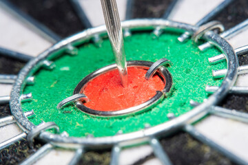 Blurred in soft focus at high magnification background with a part of an dart board with a close-up of the center (Bull's eye)with numerous holes from previous hits and an arrow stuck in the center