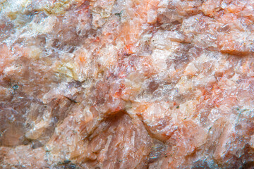 Background with the surface of a piece of red granite interspersed with quartz in soft focus under high magnification