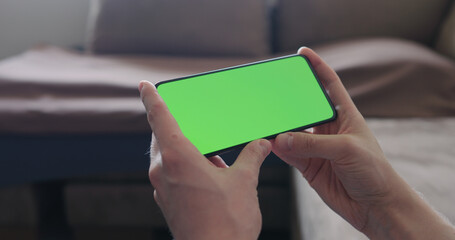 Closeup young man sit on a couch and watch something on a smartphone with green screen