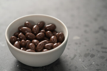 Milk chocolate dragee in white bowl on concrete background