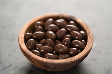 Milk chocolate dragee in olive wood bowl on concrete background