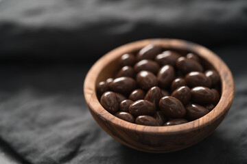 Milk chocolate dragee in olive wood bowl on linen background