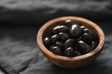 Dark chocolate dragee in olive wood bowl on linen background