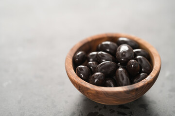 Dark chocolate dragee in olive wood bowl on concrete background