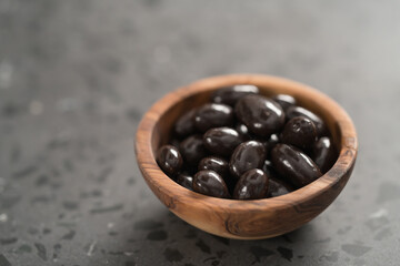 Dark chocolate dragee in olive wood bowl on concrete background