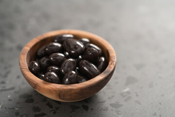 Dark chocolate dragee in olive wood bowl on concrete background