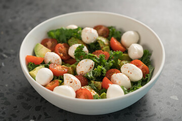 Salad with avocado, tomatoes and mozzarella in white bowl