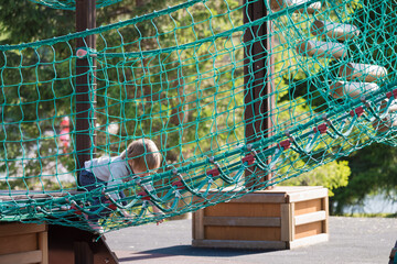 Small child plays on playground crawling in rope net.