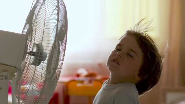 Boy Standing in Front of FBoy Standing in Front of Fan. Child Enjoying Cool Wind From Electric Fan at Home at Summer Vacation. Suffer From Heat High Temperature in Front of Ventilator Cooling Herself