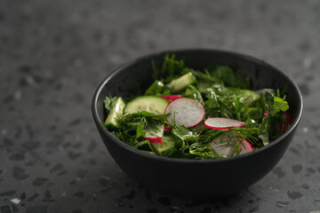 Summer fresh salad with radish, cucumber and herbs in black bowl