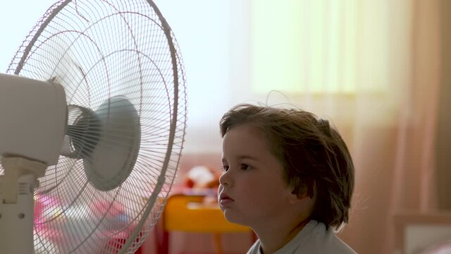 Boy Standing in Front of FBoy Standing in Front of Fan. Child Enjoying Cool Wind From Electric Fan at Home at Summer Vacation. Suffer From Heat High Temperature in Front of Ventilator Cooling Herself