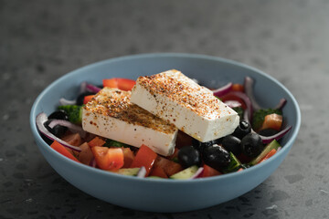 Traditional greek salad in blue bowl on concrete background