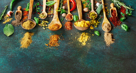 Various spice and dried herbs on dark green background. Top view of spices in wooden spoons