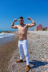 Young man in white pants and modern styling posing on the beach of the Mediterranean Sea in Burriana