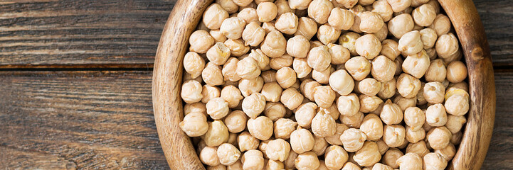 Chickpeas in a wooden bowl on the brown kitchen table. Raw chickpeas close-up. Banner with space for text