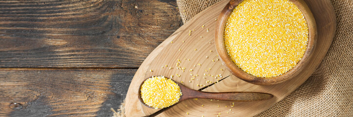Corn grits in a wooden bowl and in a wooden spoon on a brown wooden table. The view from the top....