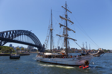 A sailing ship with tourists on board sailing at the Sydney Harbour in front of the Sydney Harbour Bridge. 