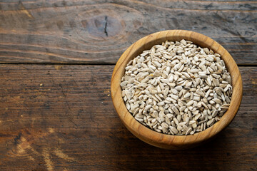 Peeled sunflower seeds in a bowl on wooden table, healthy vegan cooking ingredient.