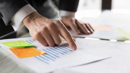 Crop close up of male employee point at graph reading consider paper company financial statistics at workplace, businessman prepare business report in office, work with paperwork finance documents