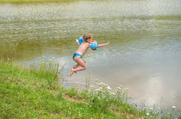 A little girl with pigtails and a blue bathing suit with a run from the shore jumps into the lake.