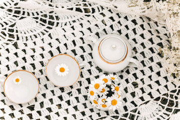 Cups, a vase with daisies and a sugar bowl on a knitted tablecloth.