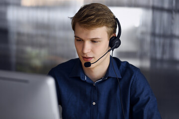 Young blond businessman using headset and computer at work. Startup business means working hard and...