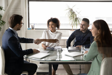 Smiling young african American woman employee shake hand of male boss director at company team...