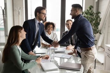 Smiling multiethnic male business partners shake hands close deal make agreement at team meeting in...