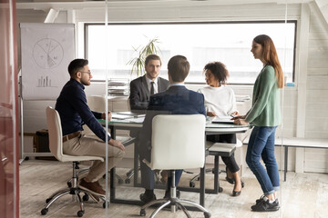 Fototapeta na wymiar Multiethnic employees gather at desk in boardroom talk brainstorm at meeting together, concentrated multiracial colleagues coworkers cooperate at team office briefing, collaboration, teamwork concept