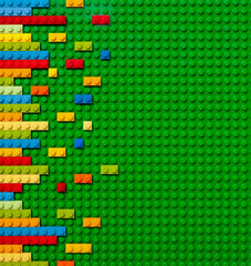 Colored toy bricks on green background © Tatsiana
