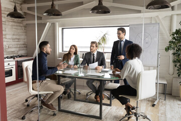 Serious young international colleagues gather in boardroom discuss company startup business plan together, multiracial businesspeople brainstorm cooperate at meeting in office, collaboration concept