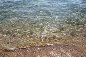 Clear sea water, sand on the beach and sun glare