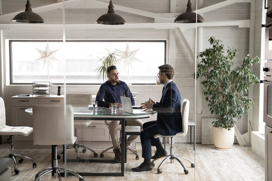 Serious multiracial young businessmen sit at desk in office talk brainstorm business startup project together, focused multiethnic male partners cooperate in boardroom at meeting, partnership concept