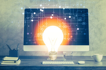 Computer on desktop in office with bulb icon hologram. Multi exposure. Concept of idea.